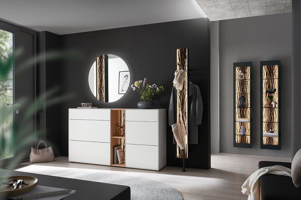 Flur mit weißer Kommode, rundem Spiegel, Garderobenpaneel und beleuchteter Vitrine