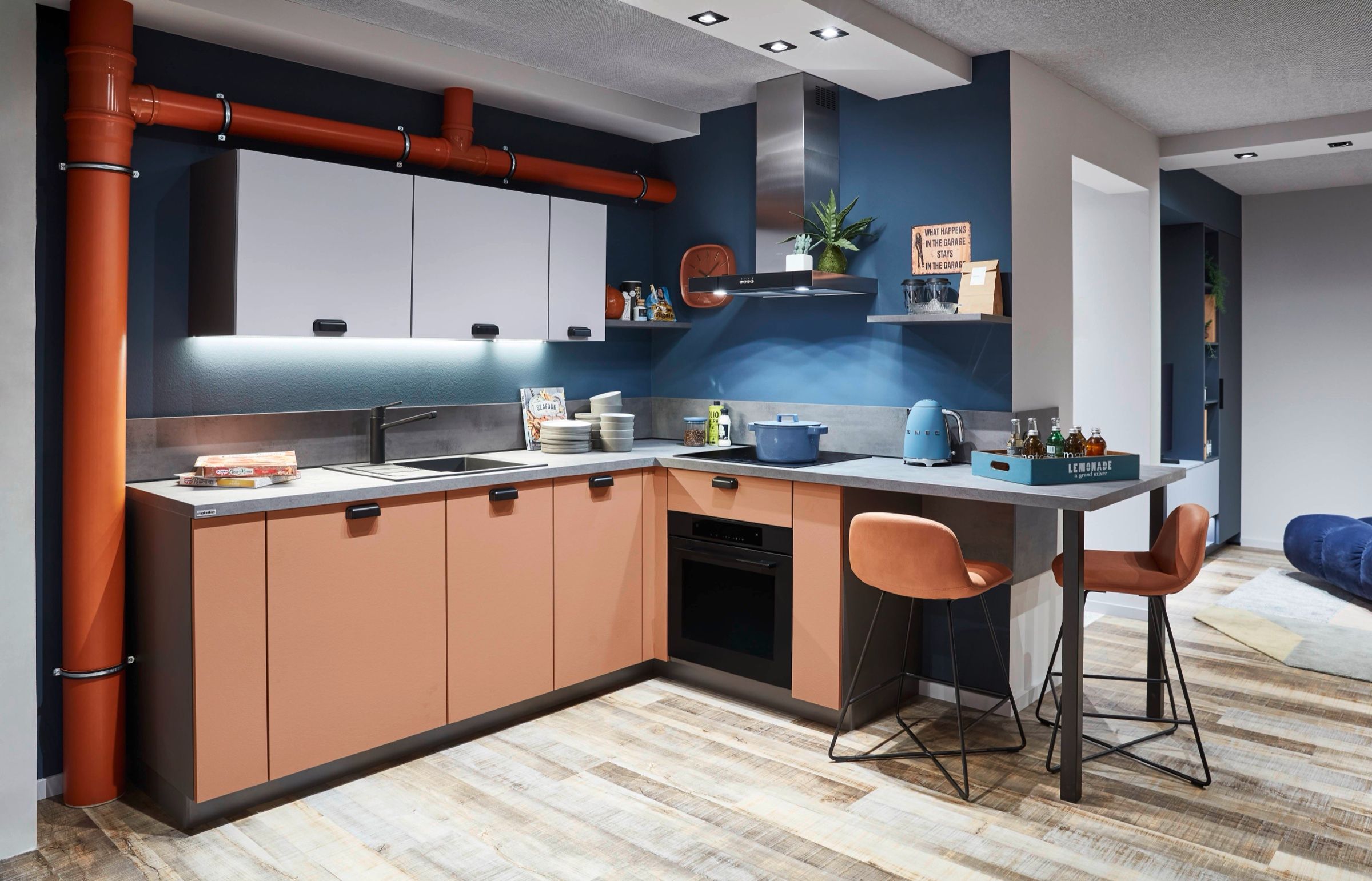 Küche mit Fronten in Terrakotta, blauer Wand und Theke mit Barhockern