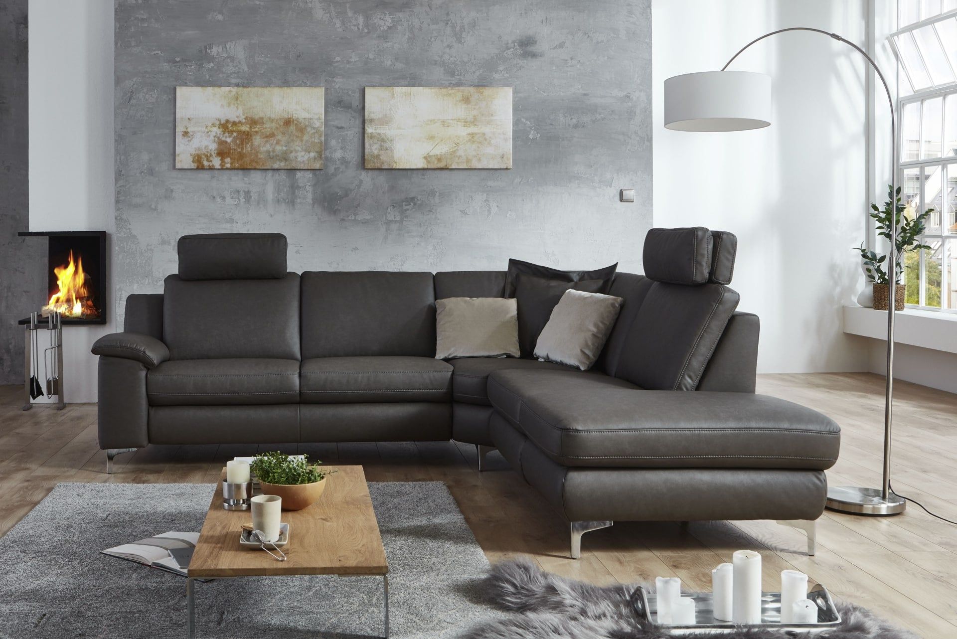 Ecksofa in Anthrazit mit Kopfstützen vor einer Betonwand mit Kamin