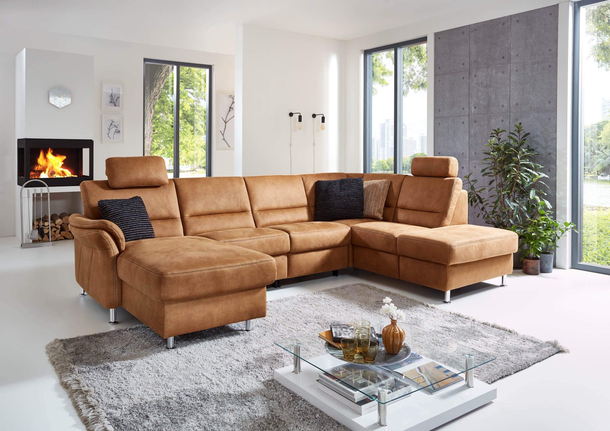 Wohnlandschaft in U-Form in Cognac mit Kopfstützen und Kissen in einem hellen Wohnzimmer mit Kamin